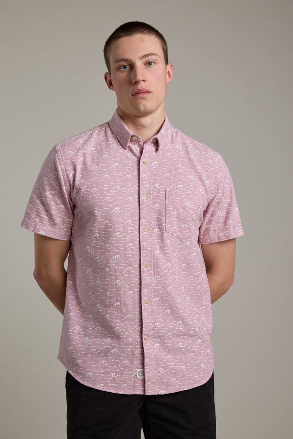 A young man with short hair wears the Barkers Shelby Print Shirt, a short sleeve summer shirt made from responsibly sourced cotton. He stands against a plain background with his hands behind his back, looking neutrally at the camera.