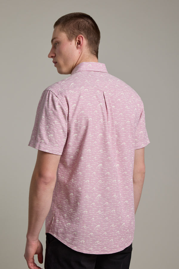 Facing away from the camera, a person with short brown hair wears the Barkers Shelby Print Shirt—a light pink short-sleeve summer shirt—and black pants, set against a plain light background.