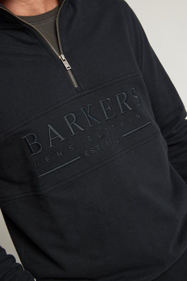 A person wearing the Barkers Heritage 1/4 Zip sweater, featuring “BARKERS MENS CLOTHING EST. 1972” embossed across the chest.