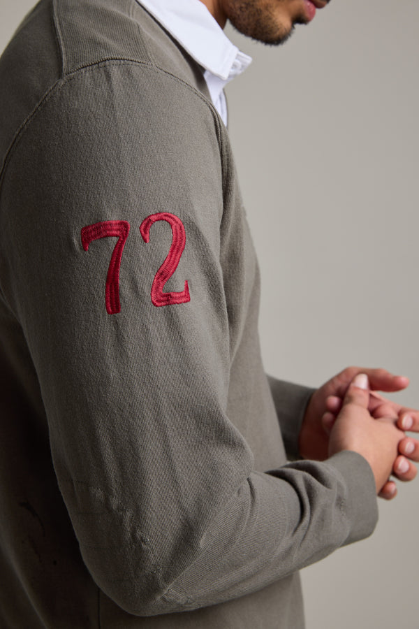 A person wearing the Barkers Stanford Long Sleeve Rugby, a gray organic cotton jersey with a red 72 embroidered on the sleeve, stands with hands clasped and only the lower half of their face showing.