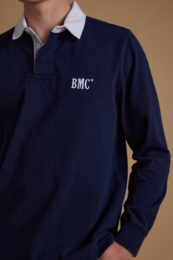 A person wearing the Barkers Stanford Long Sleeve Rugby in navy, featuring a white collar and "BMCY" printed on the left chest. The face is partially out of frame.
