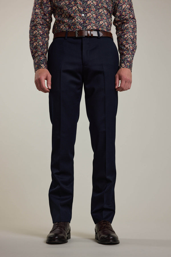 A person wears dark blue Croydon Twill Suit Trousers by Barkers, a brown belt, a floral long-sleeve shirt, and brown dress shoes, standing against a plain light background. Only the lower body is visible; upper torso and head are not shown.