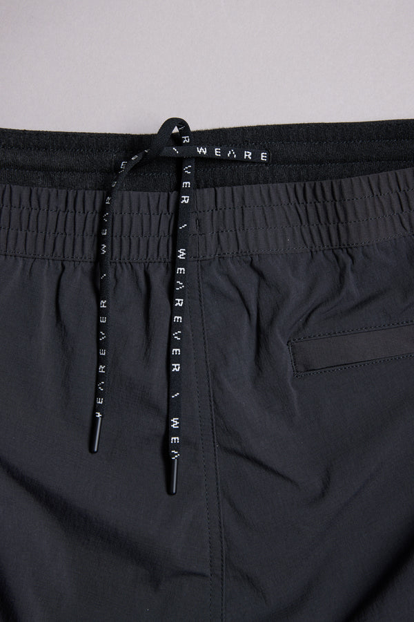Close-up of the WearEver Transit Pant's black waistband with a drawstring featuring repeating WEAR EVER text. A subtle horizontal back pocket seam is partially visible on the right side.
