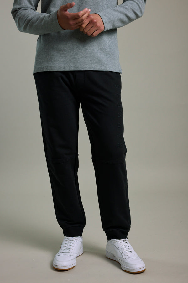 Person in a grey long-sleeve shirt, Barkers Organic Classic Print Track Pant, and white sneakers indoors.