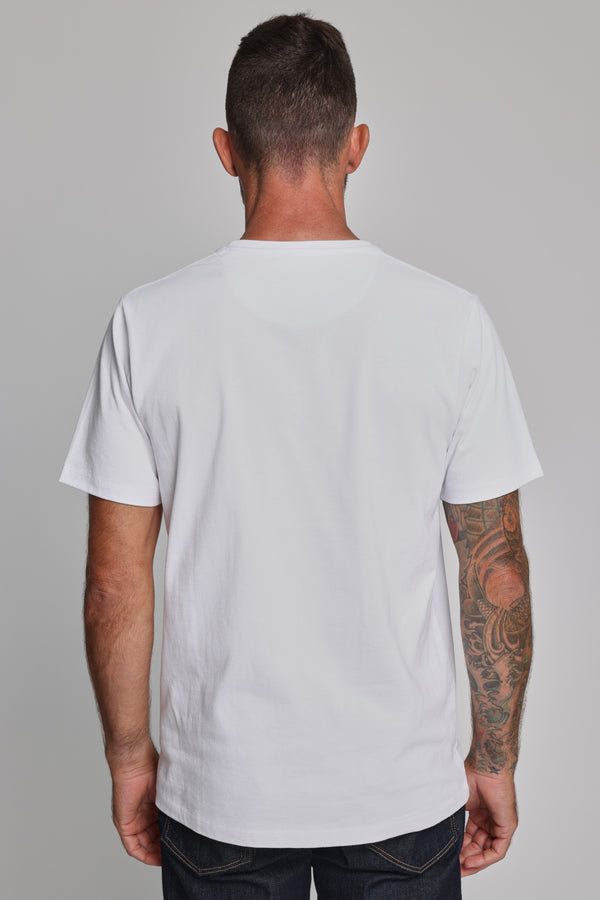 A man with short dark hair and a visible arm tattoo wears the Barkers Newton Washed Tee, an organic cotton t-shirt, standing with his back to the camera against a plain gray background.