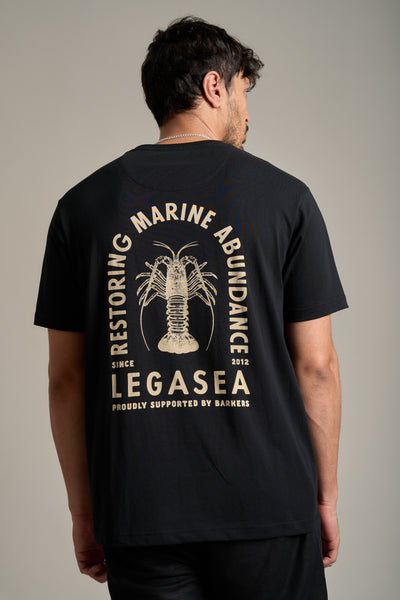 A man wears the Legasea Crayfish Print Tee, an organic cotton shirt with a bold crayfish design and "Restoring Marine Abundance," supporting New Zealand marine conservation since 2012, proudly backed by Legasea.