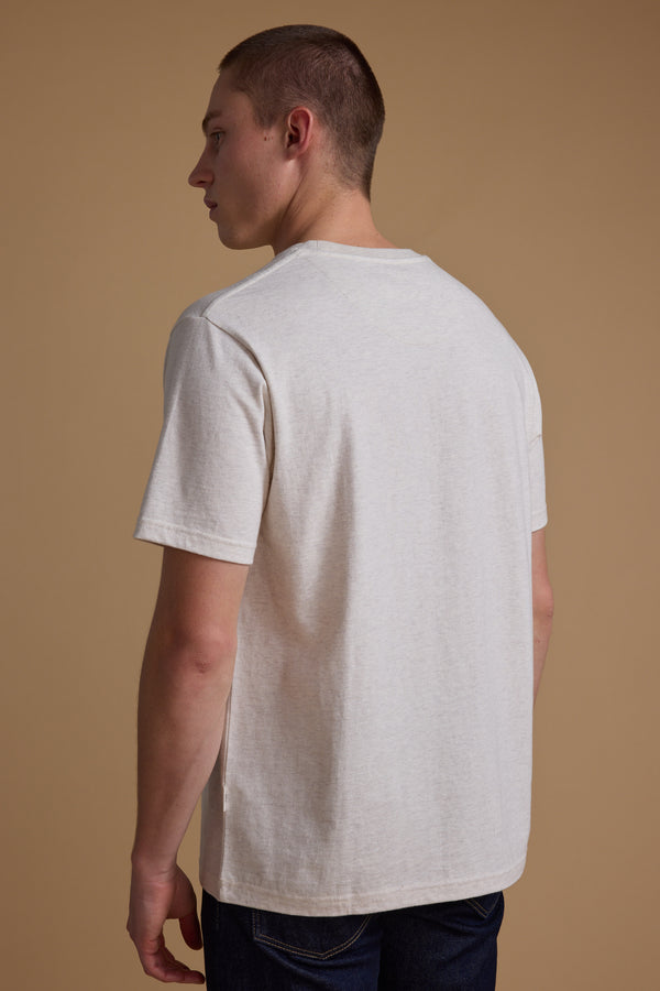 A young man with short hair faces away from the camera, wearing a light Barkers 1972 Print Tee and dark jeans, set against a beige background.