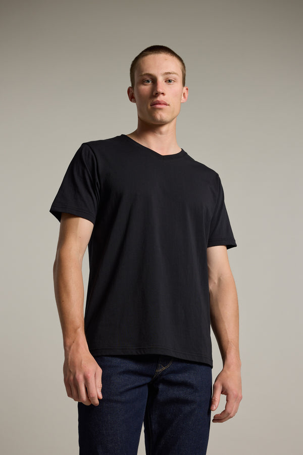 A young man stands against a plain background wearing the Barkers Organic Cotton V Neck Tee and dark jeans, confidently facing the camera with relaxed arms—a comfortable, everyday essential for effortless style.
