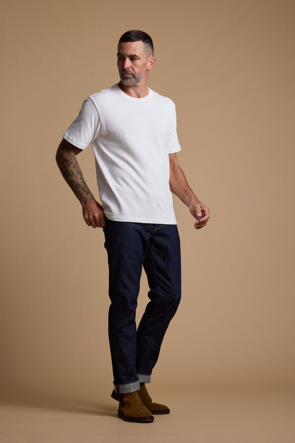Man in Barkers Langwood Tee, dark jeans, and brown boots on a plain beige background.
