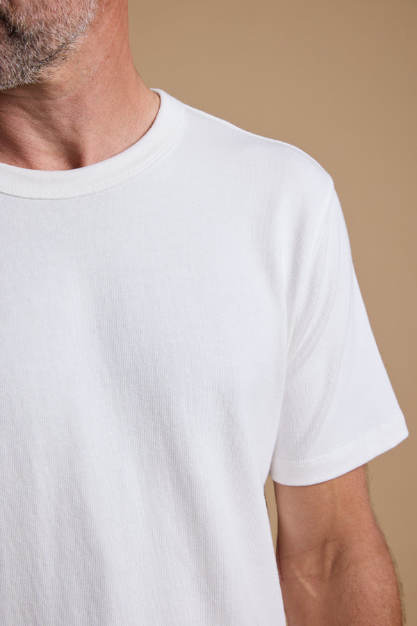 A close-up of a man wearing the Barkers Langwood Tee, a relaxed fit plain white organic cotton t-shirt, showing his neck, shoulder, and part of his trimmed beard against a beige background.