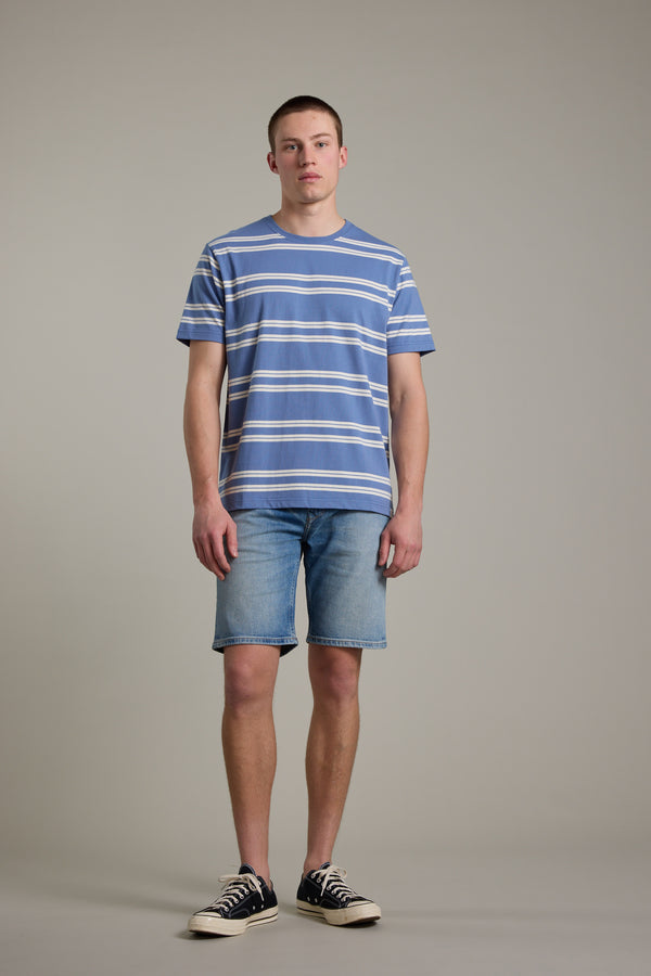 A young man stands facing forward in a blue and white striped t-shirt, Barkers Rover Denim Short in light blue, and black and white sneakers, set against a plain neutral background.