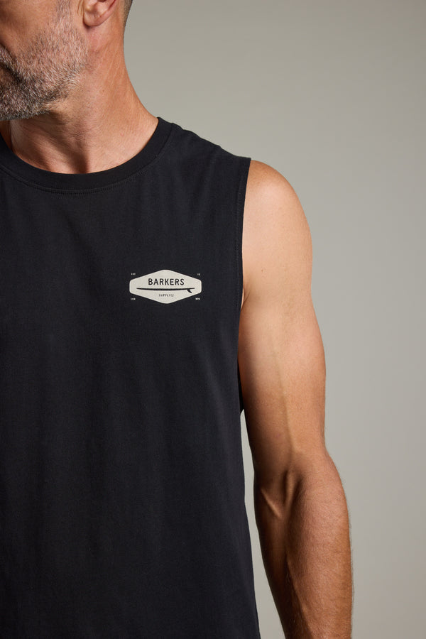 A man wearing the Barkers Supply Co Print Singlet—a sleeveless black organic cotton top with a chest logo—faces slightly left from the shoulders up against a plain background, making it a true summer essential.