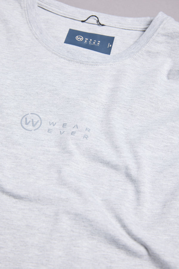 A close-up of the WearEver Outbound T-Shirt in light gray, featuring the subtle “Wear Ever” logo and text on the chest. The neckline displays a visible WearEver brand label.