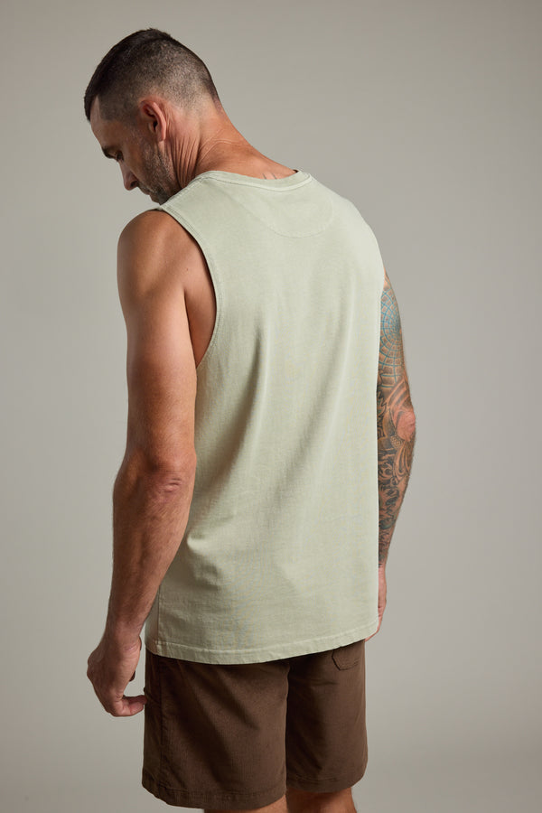 A man with short hair wears the Barkers Newton Washed Singlet in light beige and brown shorts, facing away to reveal his tattooed right arm against a plain background.
