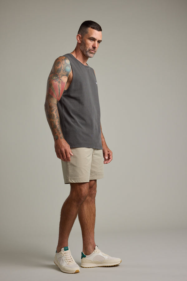 A man with short dark hair and a tattooed arm wears the Barkers Newton Washed Singlet, paired with beige shorts and white sneakers. He stands in a neutral pose against a plain light gray background, creating a subtle vintage vibe.