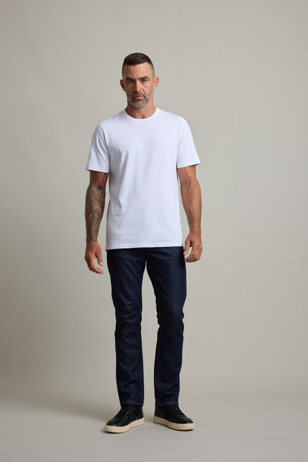 Man in Barkers Good Earth Cotton Essential Tee, dark jeans, and black shoes on plain background.