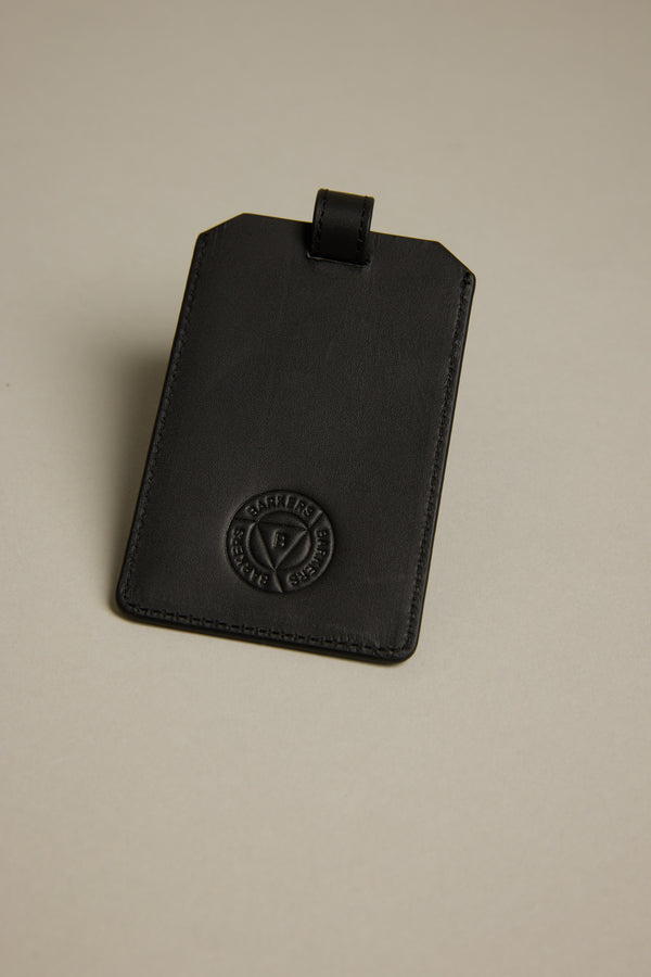 The Barkers Voyage Leather Luggage Tag, in black with a stitched circular logo near the bottom, is showcased on a light beige background—an elegant travel essential and perfect corporate gift.