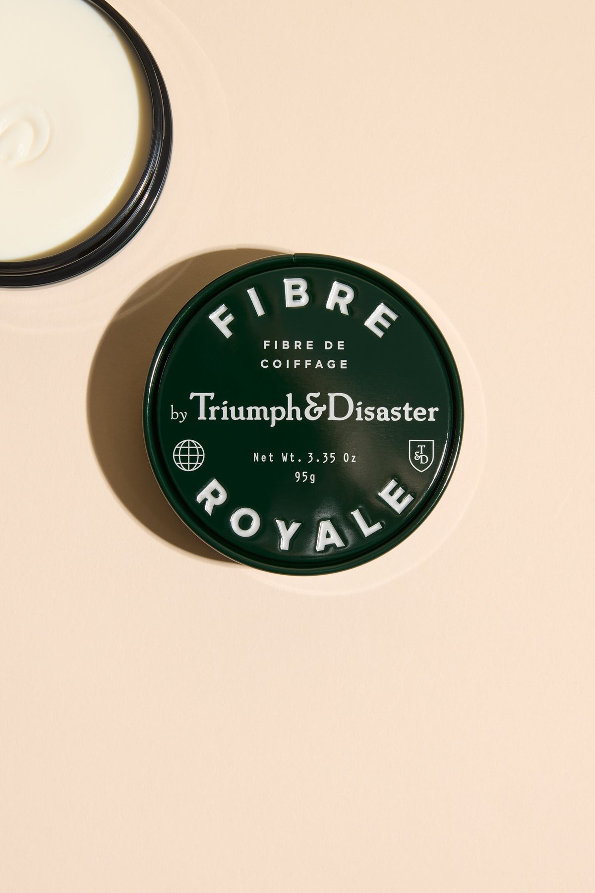 A round green tin of Triumph & Disaster Fibre Royale—a natural hair styling essential.