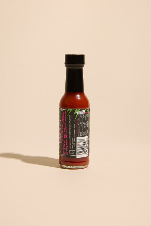 A small bottle of Culley’s Bhut Jolokia Hot Sauce with a black cap stands upright on a beige surface, its colorful label and barcode visible—perfect for adding intense heat to curries or Indian-style cuisine.