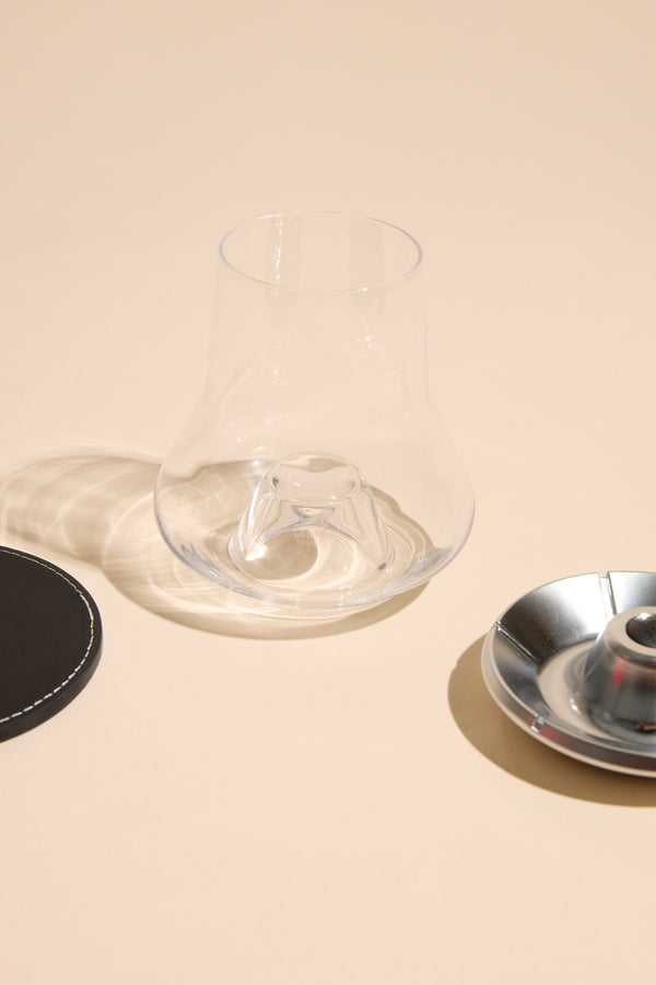 Whisky Glass Individual by Other beside a black coaster and metal dish on beige surface.