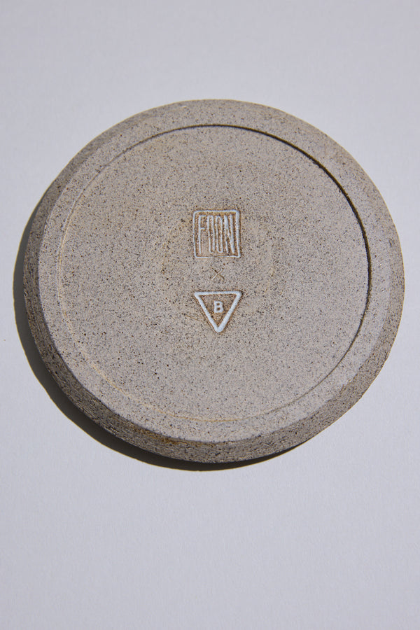 The Studio Foon Incense Dish by Other is a round, speckled New Zealand ceramic piece with a raised rim and natural clay finish, featuring a FRONT rectangle and triangle B symbol, displayed on a plain white surface.