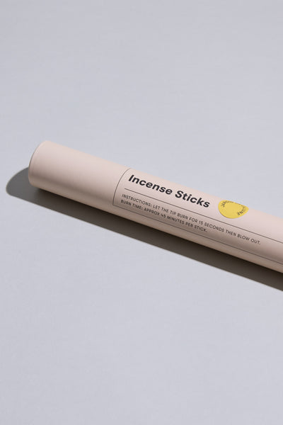 A beige cylindrical container labeled Earl of East EoE Jardin de La Lune Incense Sticks rests on a light gray surface, featuring instructions and a yellow graphic. Its soothing blackberry leaf notes are perfect for enhancing your space.