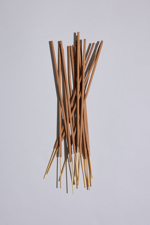 EoE Strand Incense Sticks by Earl of East, featuring brown scented sticks with golden ends, are scattered in a pile on a plain light gray background.