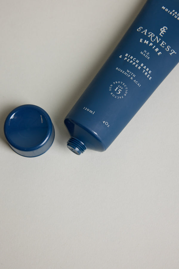 A blue tube of Other Earnest Empire SPF Moisturiser with its cap off rests on a light surface. White text highlights ingredients like birch bark and pepper tree, ideal for sensitive skin.