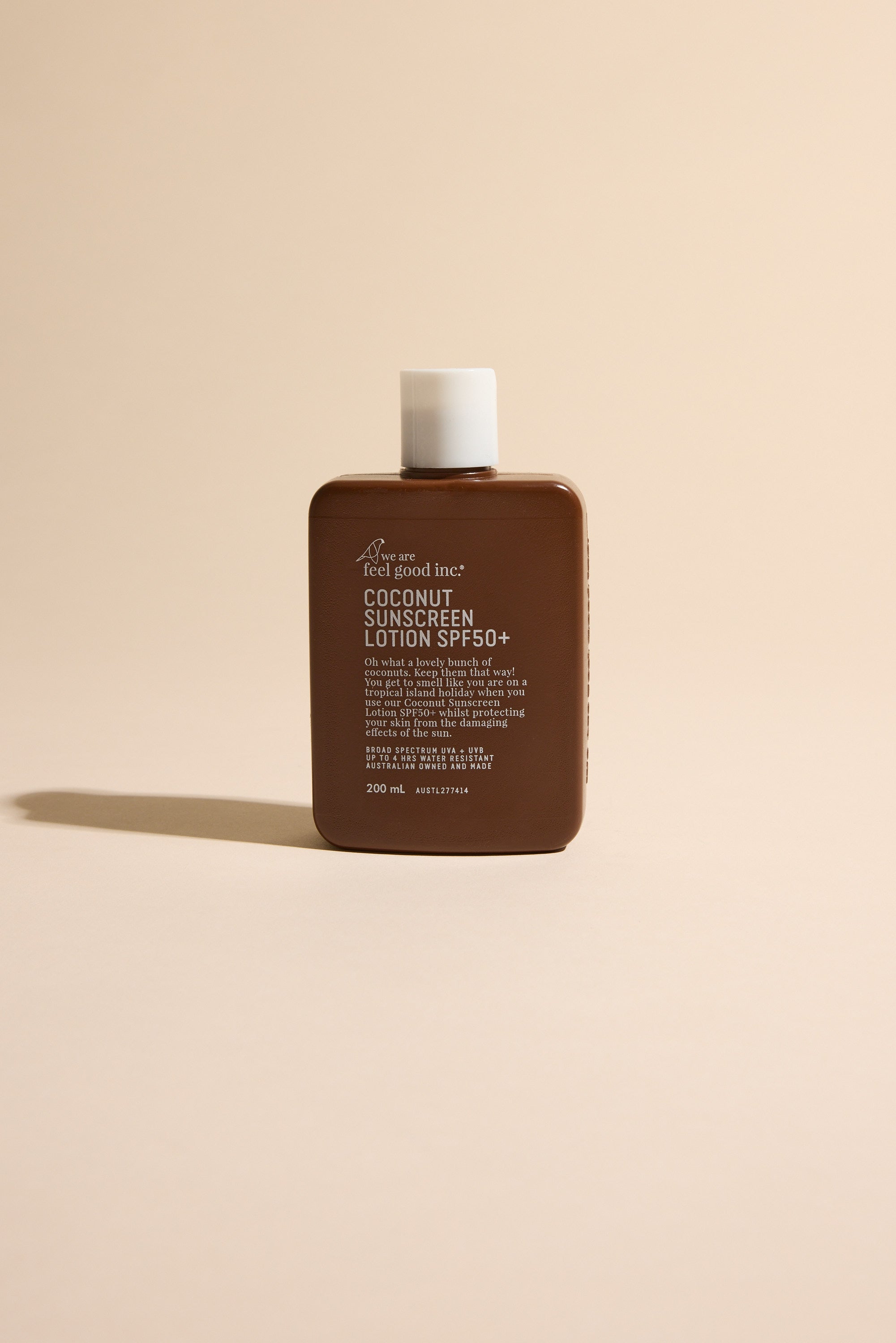 A brown rectangular bottle of Other Feel Good 50+ SPF Coconut sunscreen with a white cap stands upright on a light beige surface. The label highlights its reef safe formula in white text against a neutral background.