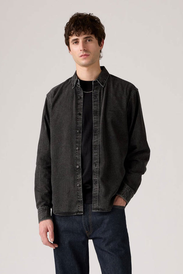 A young man with short, wavy brown hair wears a Levis Authentic Button Down Long Sleeve Shirt by Levis in black denim over a black t-shirt and dark blue jeans, standing against a plain light gray background with a neutral expression.