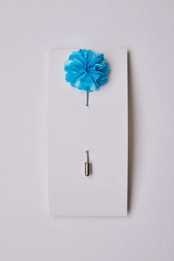 The Parisian Fraser Flower Lapel Pin, a stylish blue suiting accessory, is attached to a white card with its silver pin cap positioned below the flower.