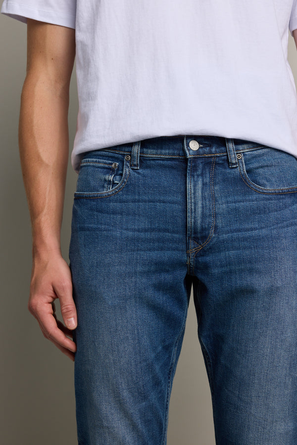 Model wearing Barkers Rambler Denim Slim Jean and a plain white t-shirt is shown from shoulders to mid-thigh, with one arm relaxed at their side against a neutral background.