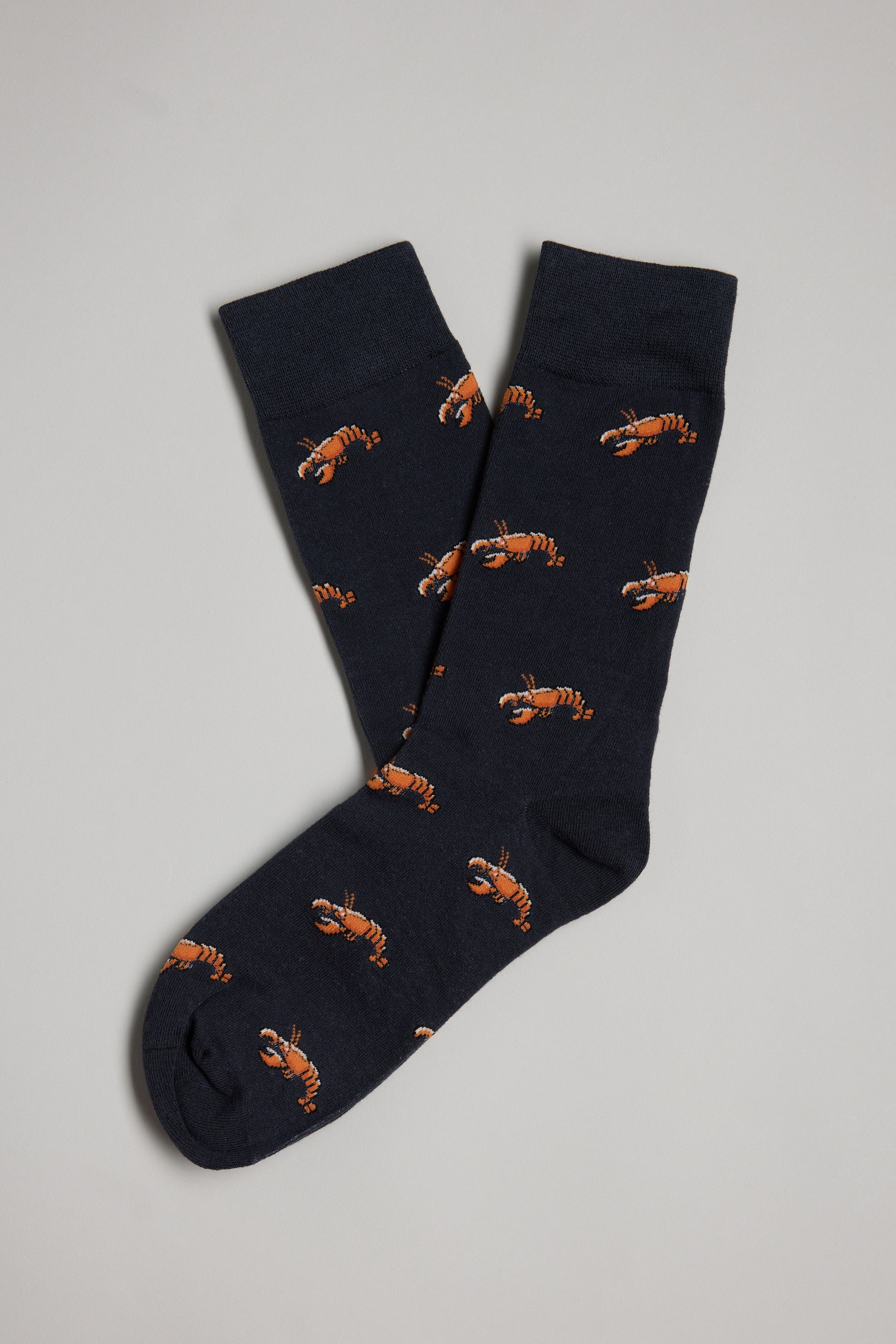 Barkers Crayfish Sock: navy blue cotton socks featuring an orange lobster pattern, laid overlapping on a light gray background. A fun and unique gift for men.