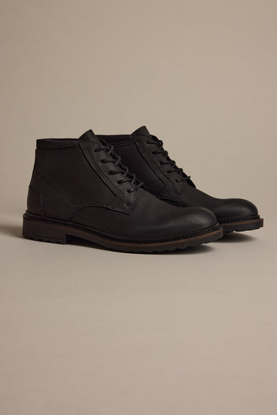 The Barkers Carlton Boot is a men's black leather luxury boot with a rugged sole, showcased on a light beige surface—a refined example of Portuguese craftsmanship.