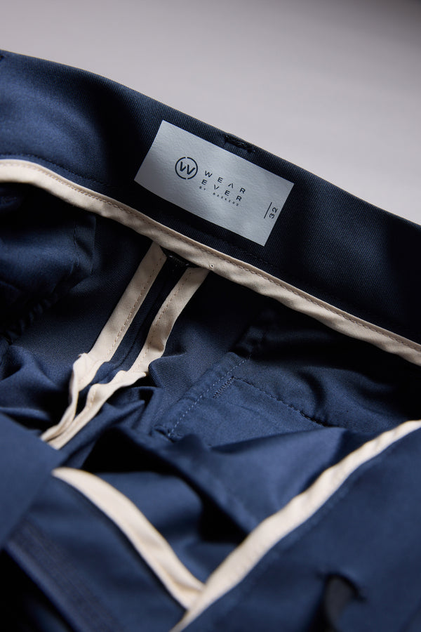 Close-up of the inside waistband of navy blue WearEver Long Game Pant, featuring a white WearEver label with size 32. Beige lining and stitching highlight its chino-inspired design.