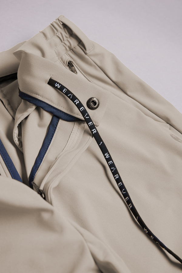A close-up of the WearEver Switch Short by WearEver shows a beige jacket with a zipper, snap button, black “WE R E V E R” drawstring, navy blue inner seam trim, and comfort stretch for easy movement.