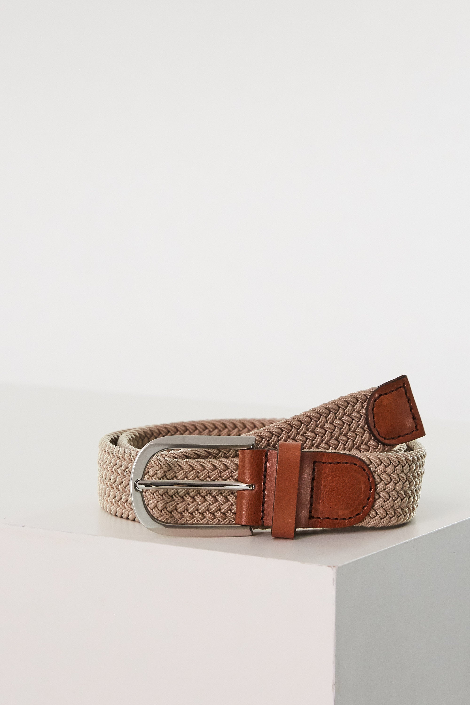 The Barkers Riviera Braided Belt, featuring beige braiding with brown leather accents and a silver buckle, is coiled neatly on a white surface, showcasing effortless summer style against a simple light background.