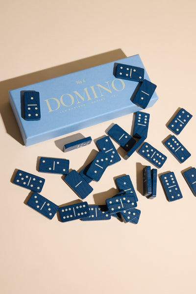 A blue box labeled "Classic Dominos" by Printworks rests on a beige surface, its lid partially open to reveal wooden domino tiles—ideal for a timeless family game night.