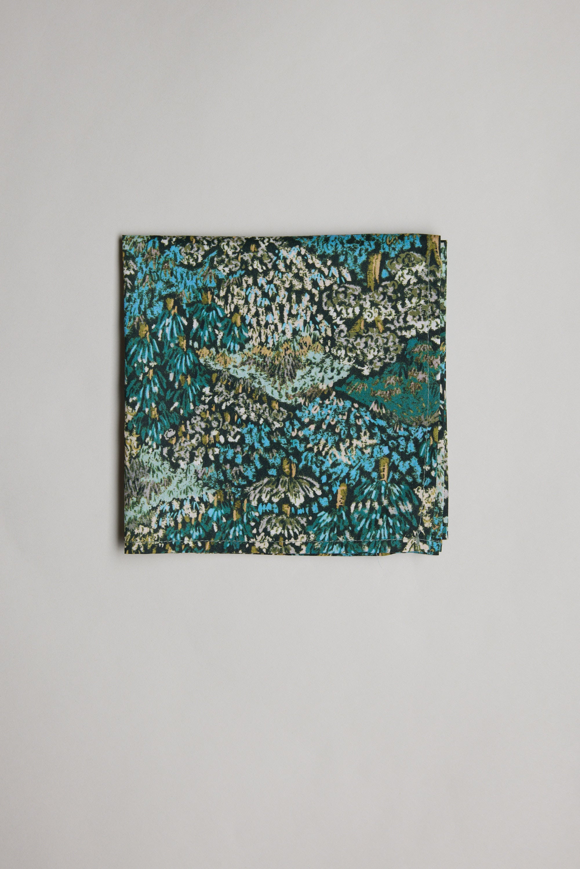 The Liberty Darley Hillside PS by Liberty is a folded rectangular pocket square in Tana Lawn cotton, showcasing a dense abstract bush print in green, blue, black, and white on a plain white background.