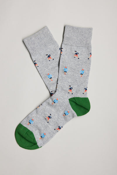 The Barkers Khyber Runner Sock is a gray cotton pair with green toes, decorated with a small repeating pattern of people in blue shirts and red pants. Shown laid flat on a light background, slightly overlapping for an everyday fit.
