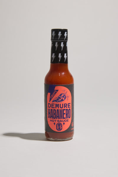 A bottle of Culley's Demure Habanero Hot Sauce has a dark label with a chili pepper illustration, inspired by classic hot sauces. It features a 3/5 heat rating and a black cap adorned with lightning bolts.