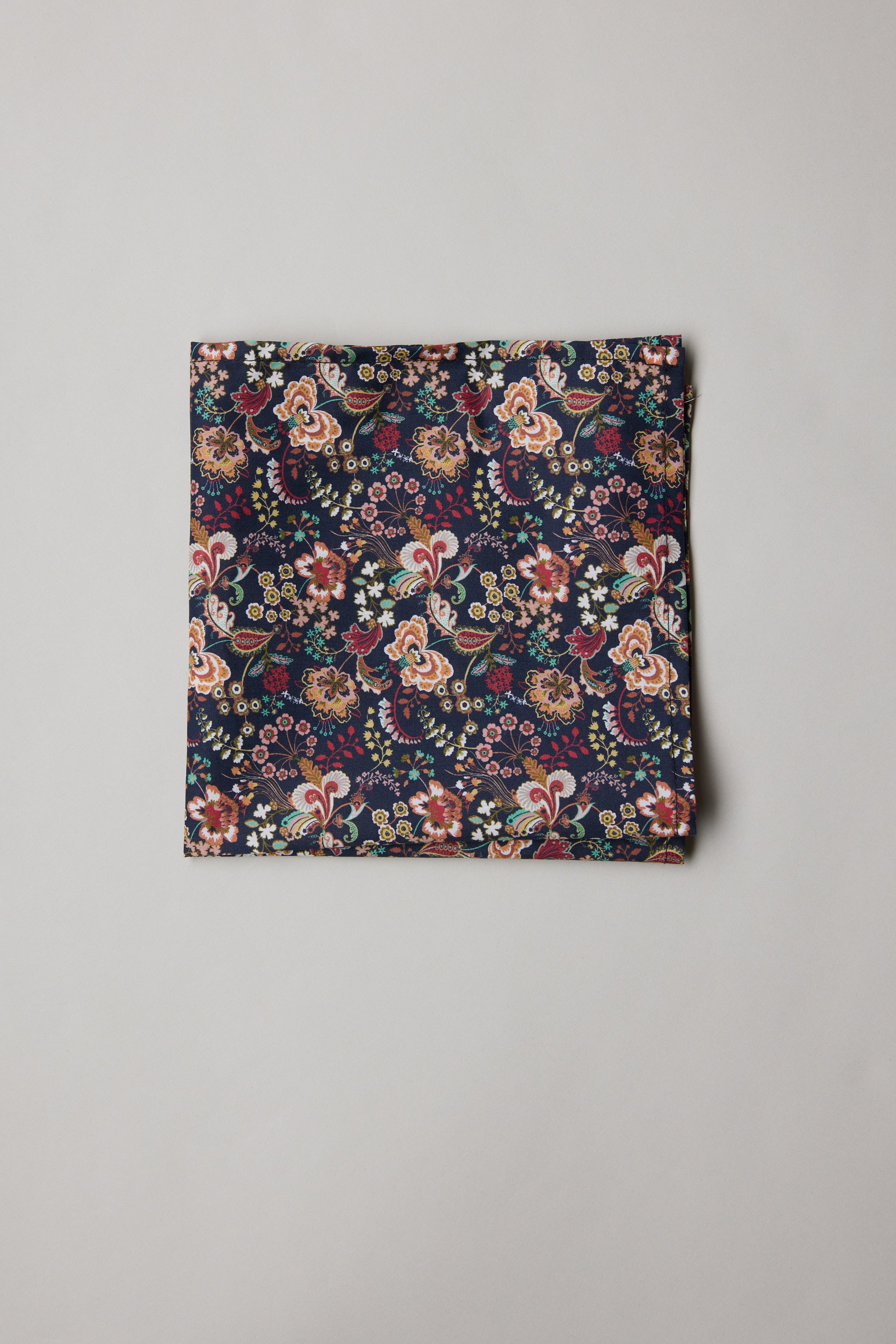 A neatly folded square of Liberty Pippa's Symphony PS Tana Lawn cotton by Liberty, featuring a colorful and intricate floral and paisley design, displayed on a plain light gray background.