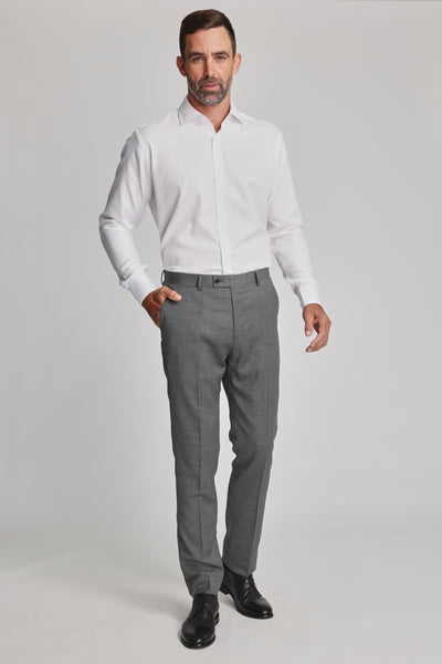 A man with short dark hair and a beard stands against a plain light background, wearing a white dress shirt, classic black shoes, and Barkers Parkland Suit Trousers. One hand is in his pocket as he poses with a neutral expression.