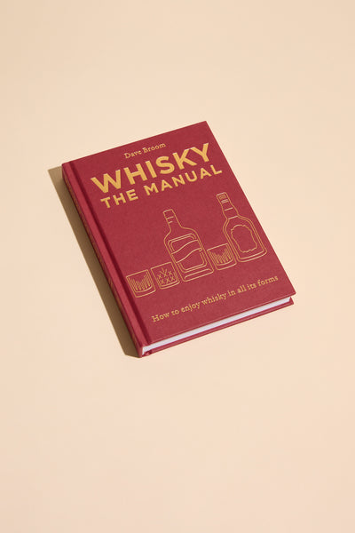 A red hardcover copy of Whisky The Manual by Other rests on a beige surface, featuring gold whisky glass and bottle illustrations—a perfect guide for learning how to enjoy whisky in all its forms.