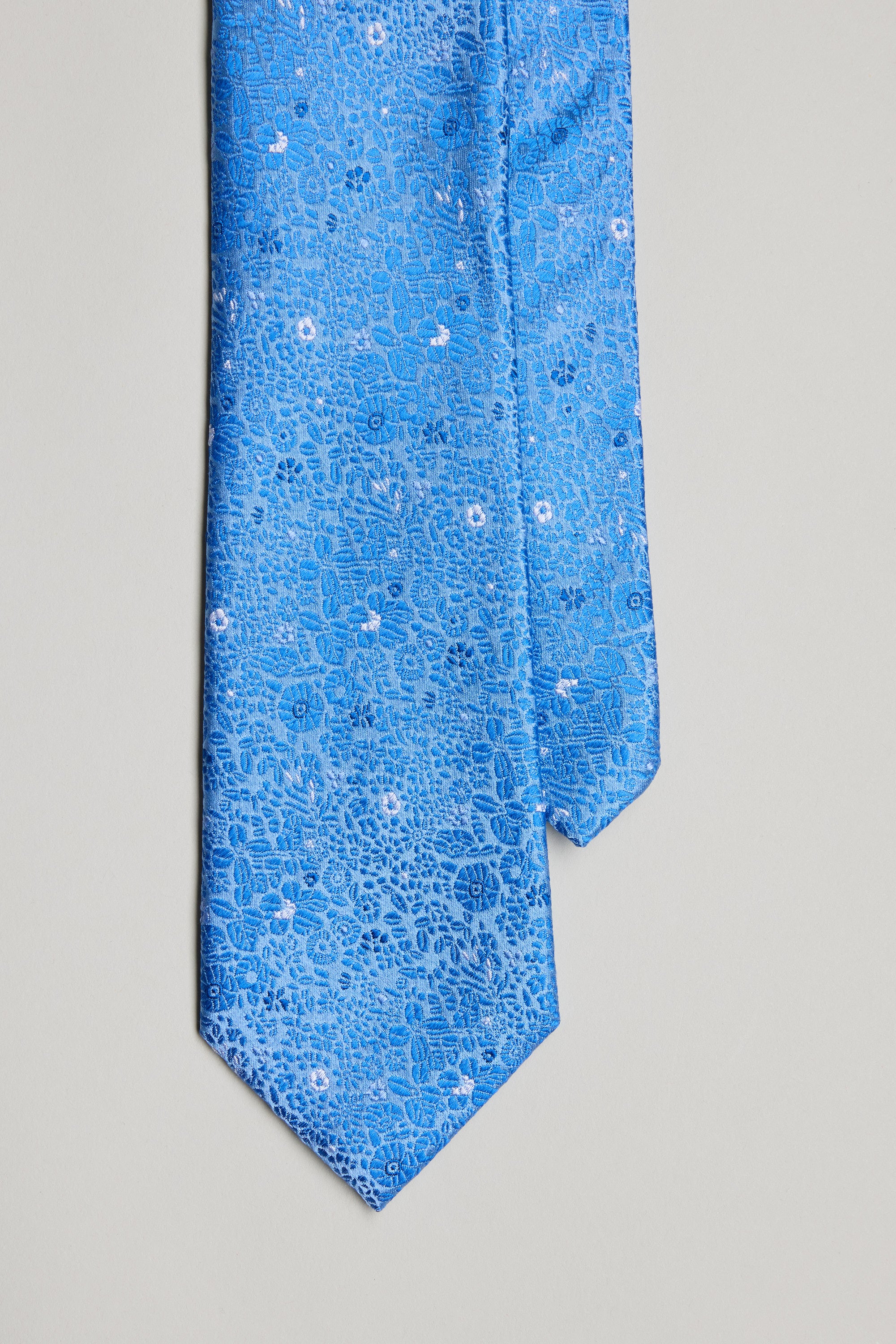 The Barkers Avery Floral Tie features a blue jacquard design with subtle white accents, shown on a light gray background—an ideal silk accessory for weddings or anyone seeking a refined look.
