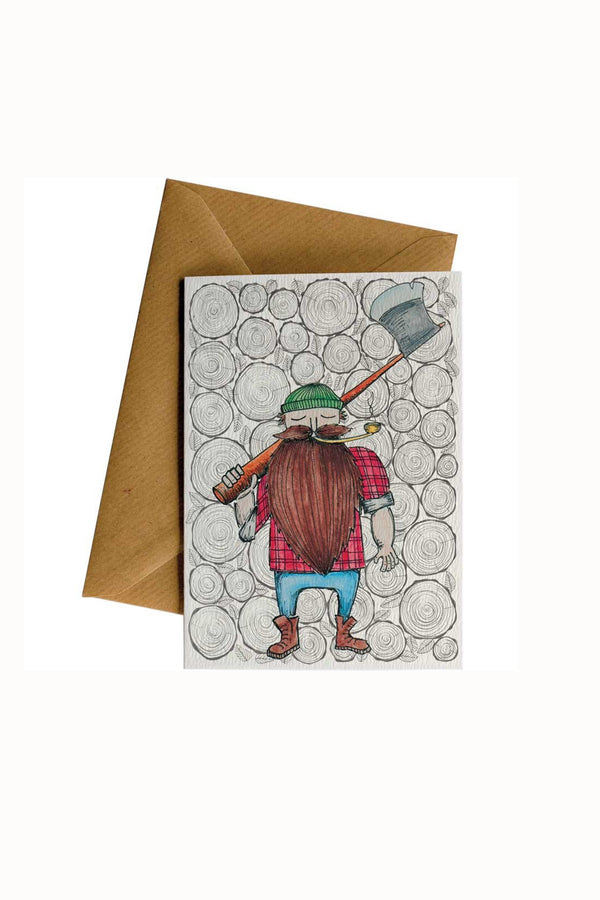 The Lumber Jack Card by Other is a recycled greeting card showing a bearded lumberjack with an axe in green hat, red shirt, and blue pants by stacked logs. Each card plants a tree and includes a brown envelope.