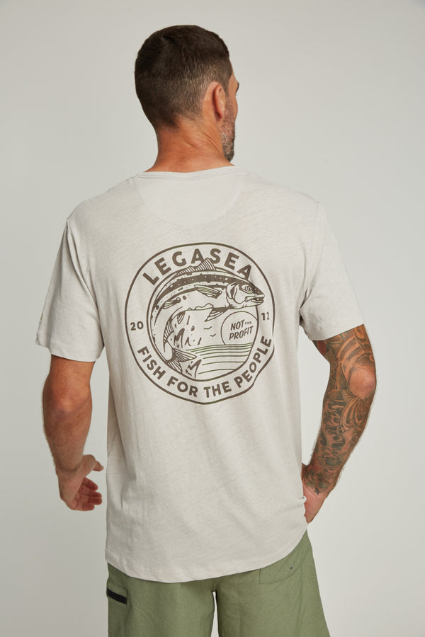 A man with short hair and a tattooed right arm is seen from behind wearing the Legasea Stamp Tee by Legasea, an organic cotton hemp shirt featuring NZ artist Blake Gordon’s fish graphic and "LEGASEA FISH FOR THE PEOPLE" text on the back.