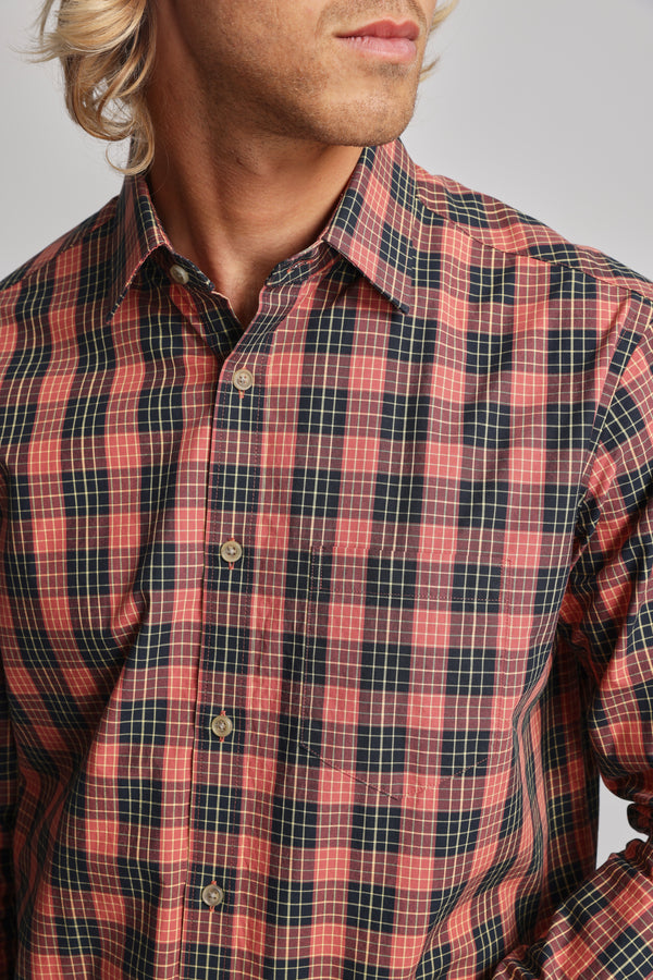A person with wavy blond hair wears the Barkers Formby Long Sleeve Shirt—a red and black plaid, classic fit style with a classic collar and beige buttons, made from responsibly sourced cotton. Shown from shoulders to above the mouth.
