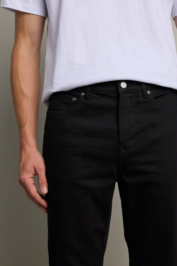 A person is shown from waist to mid-thigh wearing a white t-shirt and Barkers Rambler Denim Slim Jean, with one arm relaxed at their side against a neutral background.