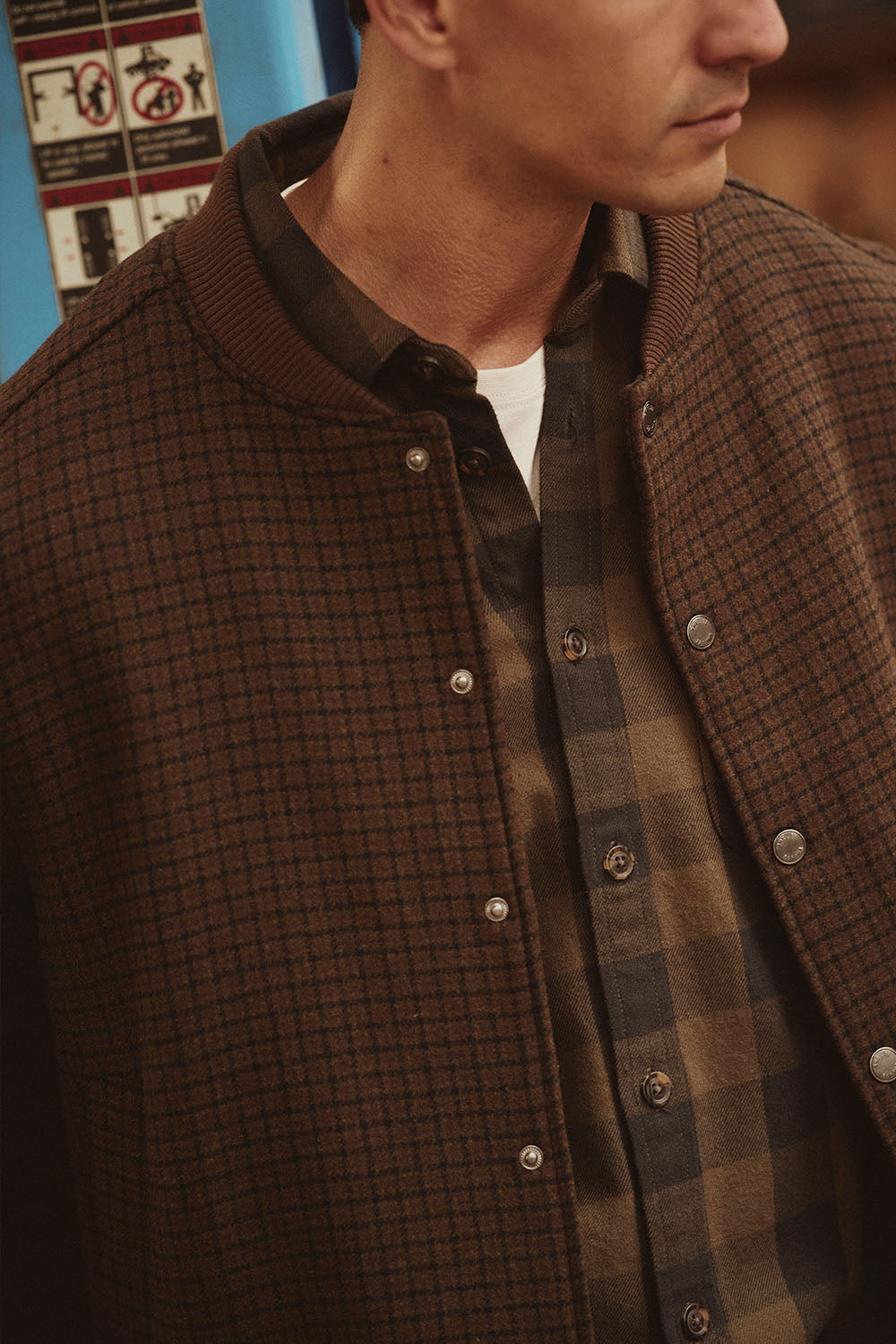 Man wearing a brown checkered jacket over a plaid shirt, channeling classic NZ style.